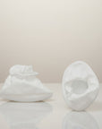 Two white ceramic sculptures on a reflective surface with a neutral background