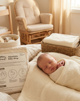 Newborn baby wrapped in a beige blanket with 'Mother's Choice' adjustable baby wrap packaging in a nursery setting.