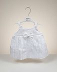 White baby dress with a bow on a hanger against a beige background