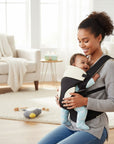Stork And Baby brown 3-way baby carrier with adjustable straps, worn by a smiling mother holding her baby.