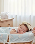Stork And Baby cream satin Alice band with a large bow and pearl embellishments worn by a sleeping baby in a bassinet