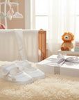 Stork And Baby Mothers Choice white christening booties with rose detail, presented in a gift box on a soft rug.