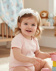Stork And Baby girls Alice band featuring white flowers and pearl accents worn by a smiling toddler in a nursery.
