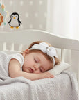 Stork And Baby white alice band with bow and diamante detail worn by a sleeping baby in a nursery
