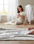 Stork And Baby 5 piece newborn starter set in Grey Elie, including a bib, hat, mittens, grower, and bodysuit with a blue ribbon.