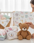 Stork And Baby pink, blue, and mint green baby blankets and a cutwork blanket with pink birds and bottles. A teddy bear sits nearby.