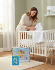 Stork And Baby blue cutwork blanket with airplane and cloud motifs for infants. A woman is placing a unicorn-print blanket on a crib.