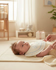 Stork And Baby infants towelling dribble bibs with blue trim and teddy bear print, on a baby lying on a cream mat.