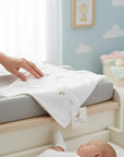 Stork And Baby Mothers Choice beige cotton jersey wrap being touched by a hand in a cozy nursery setting.