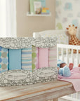 Stork And Baby Mothers Choice 3 pack muslin wraps in blue and pink patterns on a wooden table in a nursery.