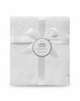Stork And Baby Mothers Choice white knitted baby shawl with cable pattern, tied with a ribbon and gift tag.