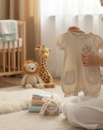 Stork And Baby beige muslin romper with embroidered bunny and lavender, featuring ruffled pockets and sleeves.