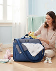 Stork And Baby Navy Combo Nappy Bag with multiple compartments and organized storage. A woman is placing a yellow toy bear on top.