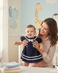Stork and Baby navy sailor short sleeve dress with white trim and bow for infant girls. Mother holds smiling baby.
