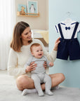 Stork And Baby navy sailor dungaree set for infant boys, featuring white top with blue trim and bow tie, navy shorts with suspenders.