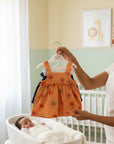 Stork And Baby: Orange sleeveless baby dress with sun print and ruffle hem, paired with denim shorts.