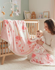 Stork And Baby pink and white infants cutwork blanket with house and tree print. A mother holds her baby next to a crib.