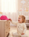 Stork And Baby bright pink cotton cap with 'Princess' embroidered on the front, shown with a smiling baby girl.