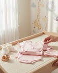Stork And Baby pink cotton romper with "Born To Shop" graphic, matching bib, hat, booties, and wooden toy.