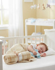 Stork And Baby beige plaid polar fleece receiver blanket rolled and tied with a ribbon, covering a sleeping baby in a crib.