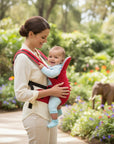 Stork And Baby red 3-way baby carrier with adjustable straps, holding a smiling baby in a garden setting.