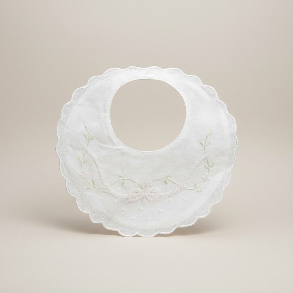 White baby bib with floral embroidery on a beige background