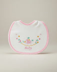White baby bib with pink trim and floral embroidery on a beige background