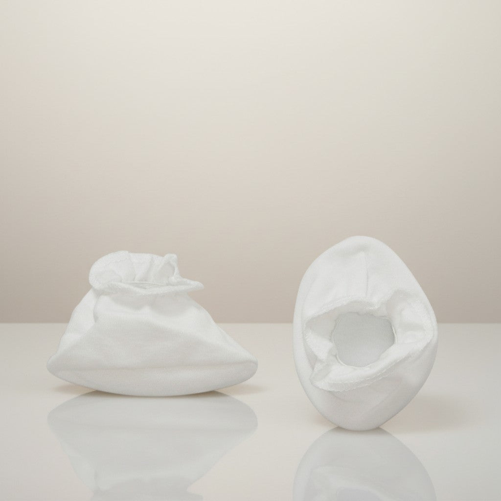 Two white ceramic sculptures on a reflective surface with a neutral background