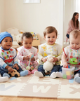 Group of toddlers sitting on a rug with toys in a bright room