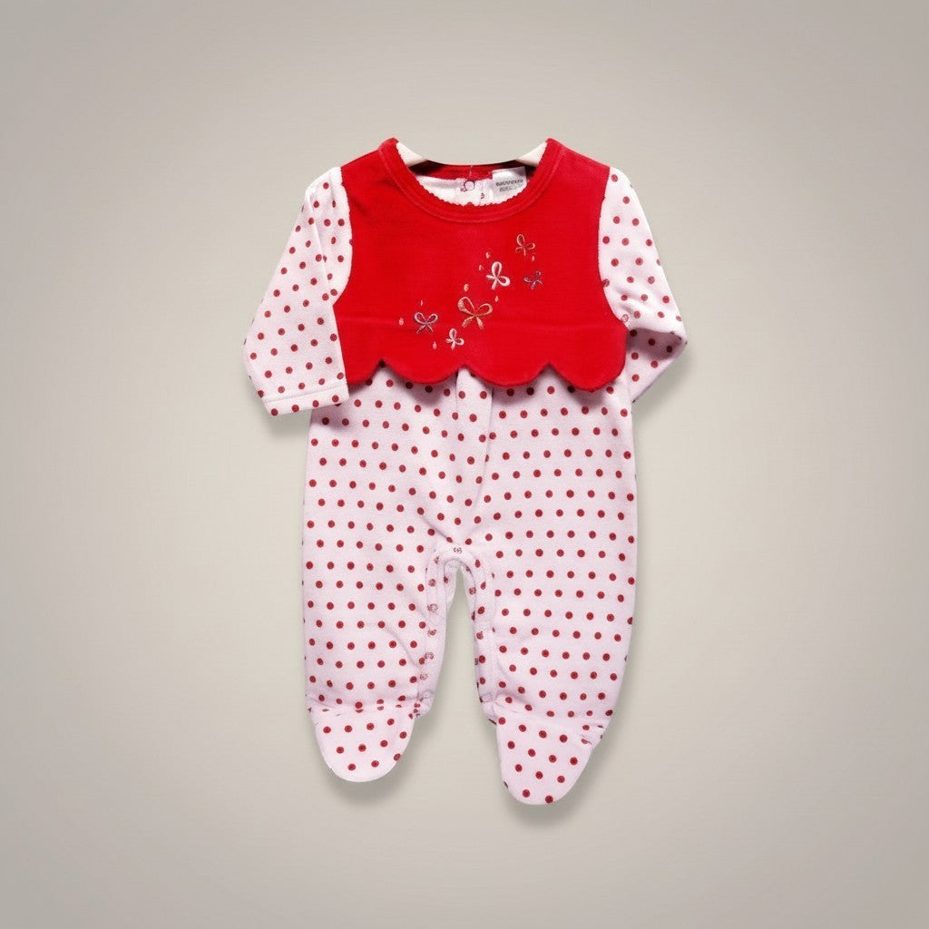 Baby onesie with red top and white polka dot bottom on a gray background
