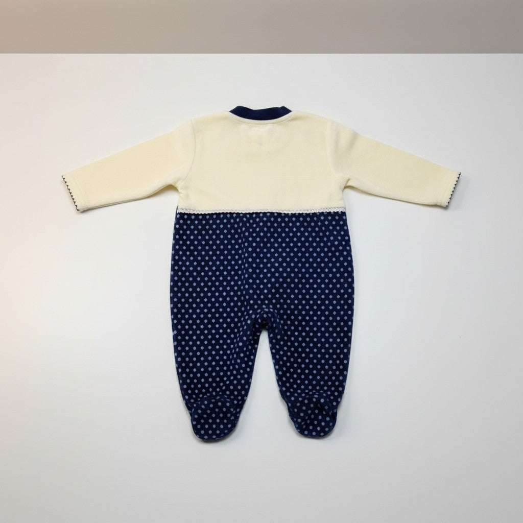 Baby onesie with cream top and navy polka dot bottom on a white background