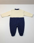 Baby onesie with cream top and navy polka dot bottom on a white background