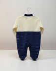 Baby outfit with cream top and navy polka dot pants on a hanger against a light background