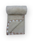 Folded beige blanket with brown checkered border on a white background