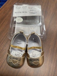 Gold children's shoes with heart designs in a clear plastic packaging on a wooden surface.