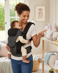 Stork And Baby black polka dot 4-way baby carrier worn by a smiling mother holding her baby. Soft fabric.