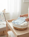 Stork And Baby light blue 100% cotton babygrow with embroidered detail, laid in a woven basket.