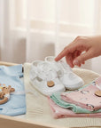 Stork And Baby white fabric christening booties with car embroidery detail, displayed on a wooden changing table.