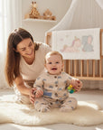 Stork And Baby boys muslin romper in beige with blue rainbow print, featuring a button front and blue accent pocket.