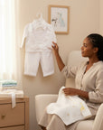 Stork And Baby white christening suit for boys with long sleeves, vest, and bow tie, held by a woman in a nursery.