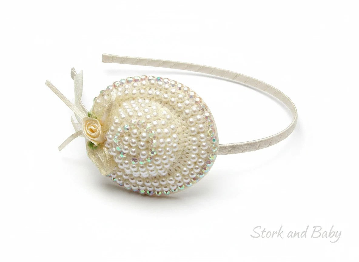 Stork And Baby cream girls alice band featuring a miniature hat adorned with pearls, iridescent beads, and a ribbon rose
