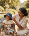 Stork And Baby dark blue denim bucket hat on a smiling baby in a stroller, with a woman adjusting the hat.