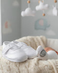 Stork And Baby white embroidered christening booties for baby girls with velcro strap, resting on a knit blanket.