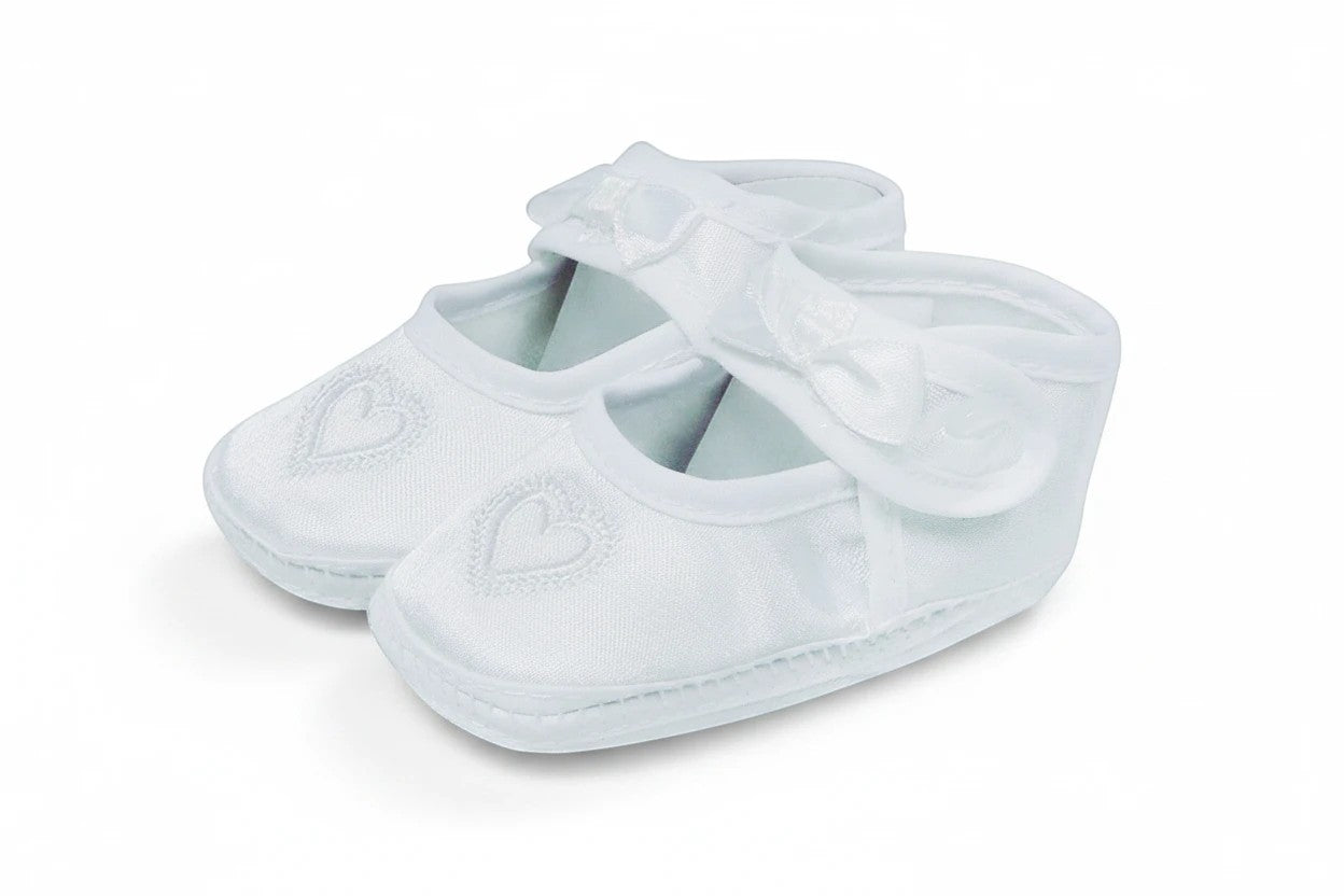 Stork And Baby white satin christening booties for girls featuring embroidered heart detail and a delicate bow strap.
