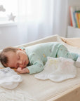 Stork And Baby white lace socks for girls with assorted bows, displayed on a changing table next to a sleeping baby.