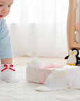 Stork And Baby white lace socks for girls featuring assorted decorative bows, worn by a baby in a nursery setting.