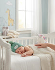 Stork And Baby green knitted pom pom beanie with "mother's choice" patch on sleeping baby.