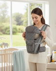 Stork And Baby grey polka dot 4-way baby carrier with padded straps and adjustable buckles. Woman wearing carrier in nursery.