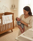 Stork And Baby mother holding a smiling infant in a striped romper, nursery setting with crib and changing table.