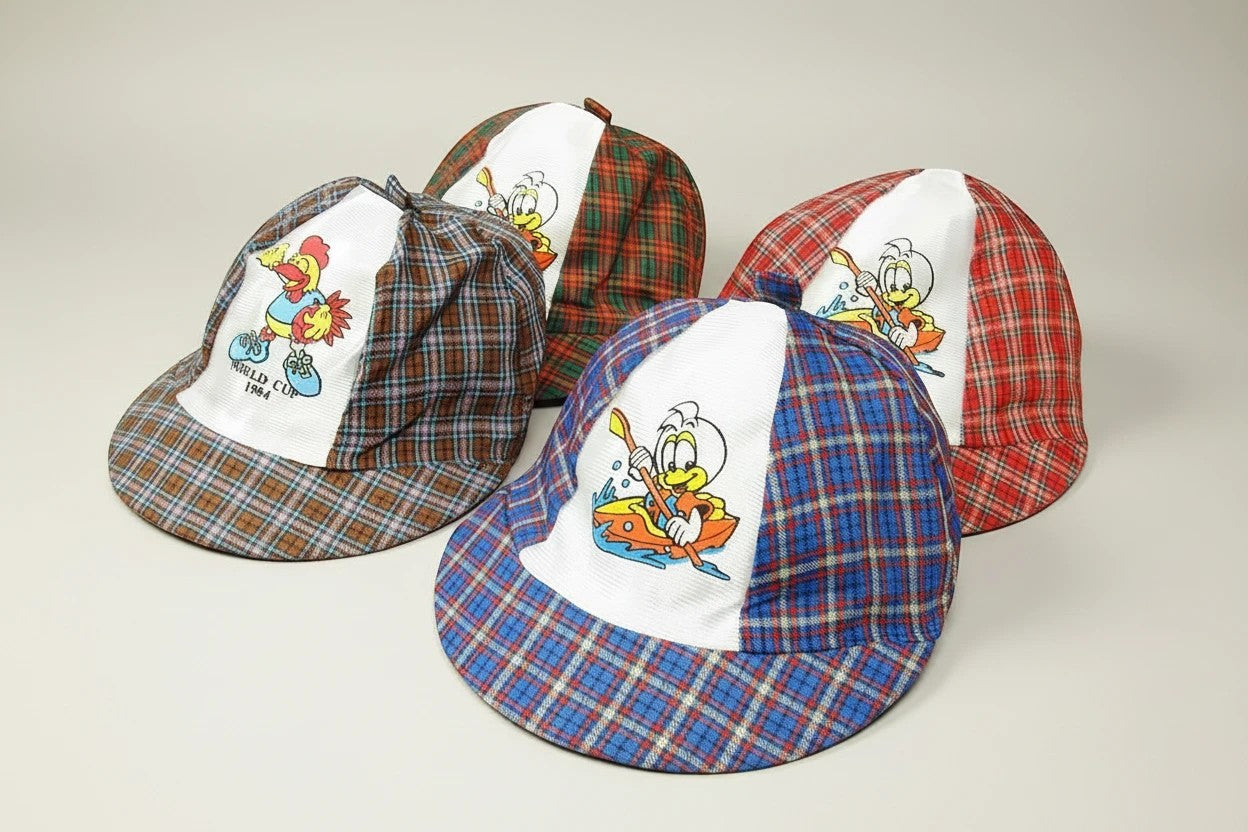Stork And Baby infant boys check caps in plaid with cartoon ducks and chickens. Available in red, blue, and brown.